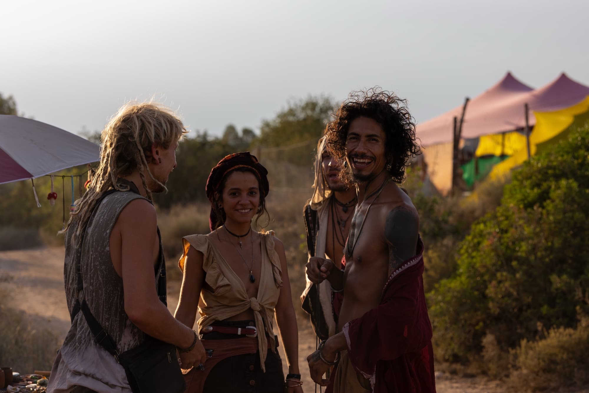 Three friends talking in warm golden hour light between festival tents