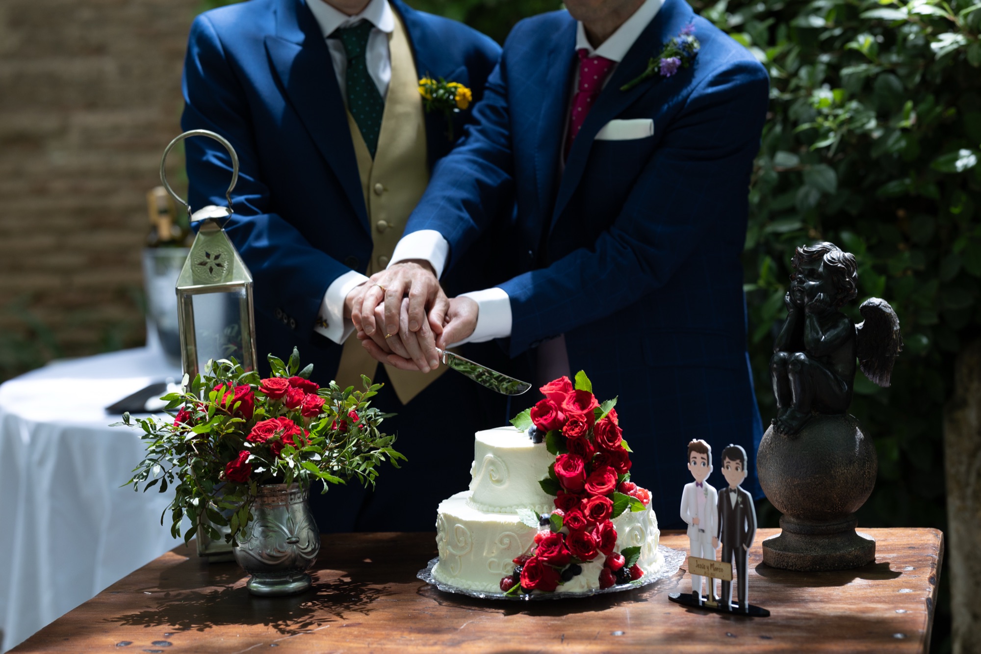 Two grooms cutting their wedding cake together, red roses on white icing
